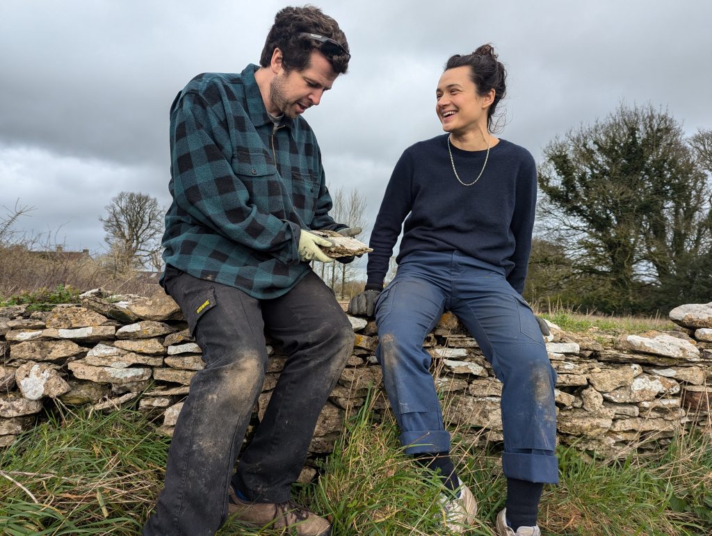 Joe and Leah sitting on a dry stone wall in the Cotswolds