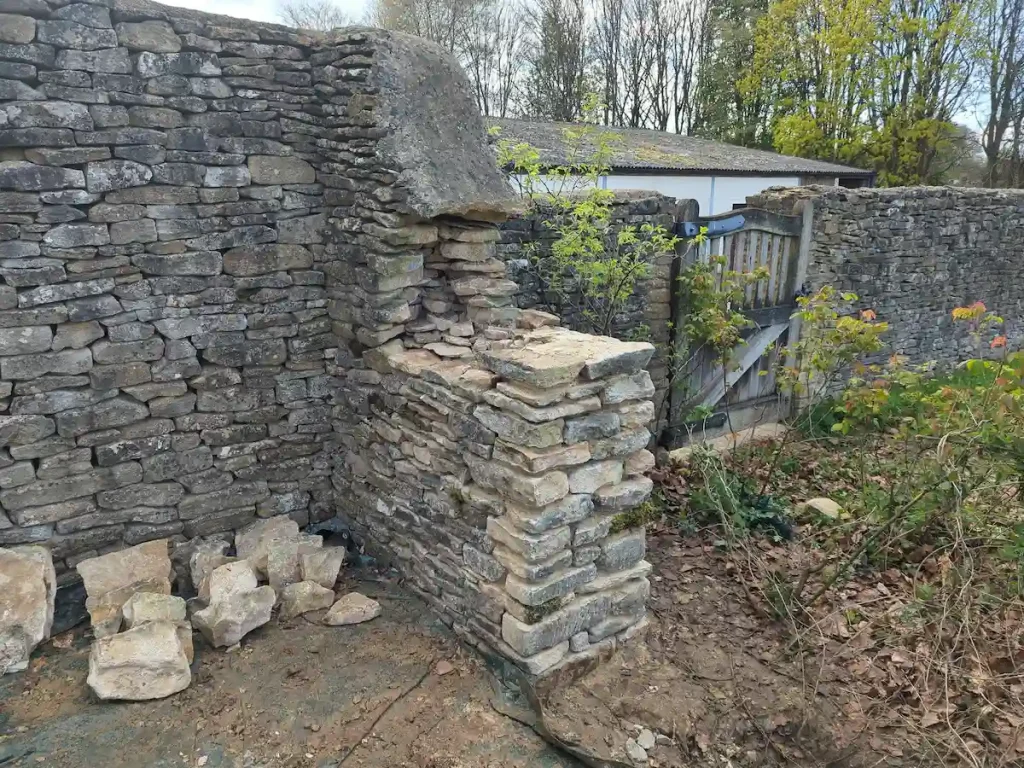 Dry stone wall builder completing shortening of a dry stone wall with a lime mortared wall head in Sherston near Tetbury.