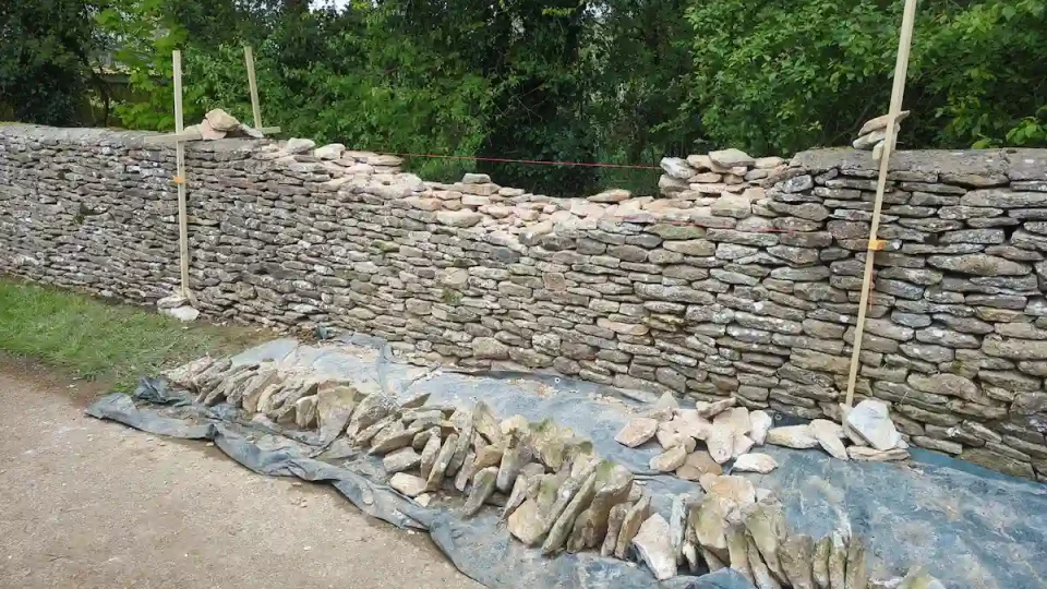 Traditional dry stone walling repairing a bulging agricultural field wall in Tetbury, Gloucestershire.